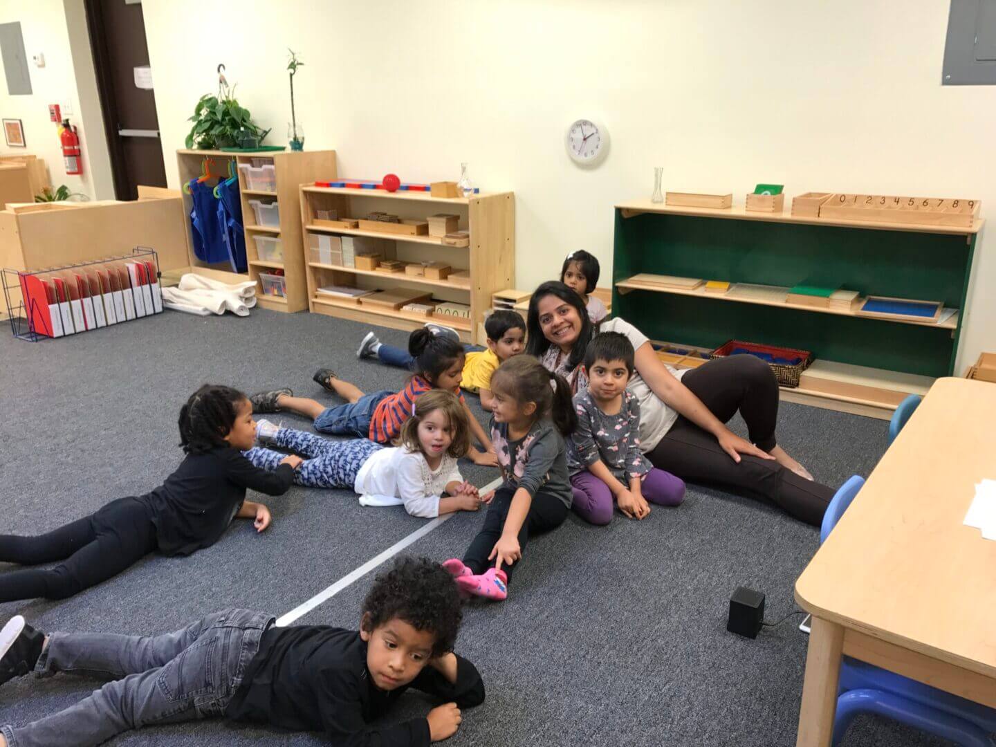 A group of children and a teacher playing together on a classroom floor.
