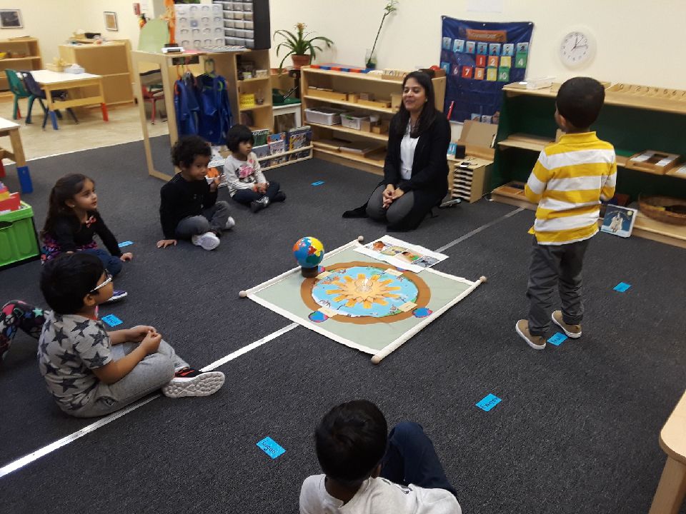 Children and teacher engaged in a classroom activity sitting around a world map.