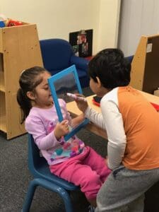 Two children engaging with a mirror in a classroom setting.