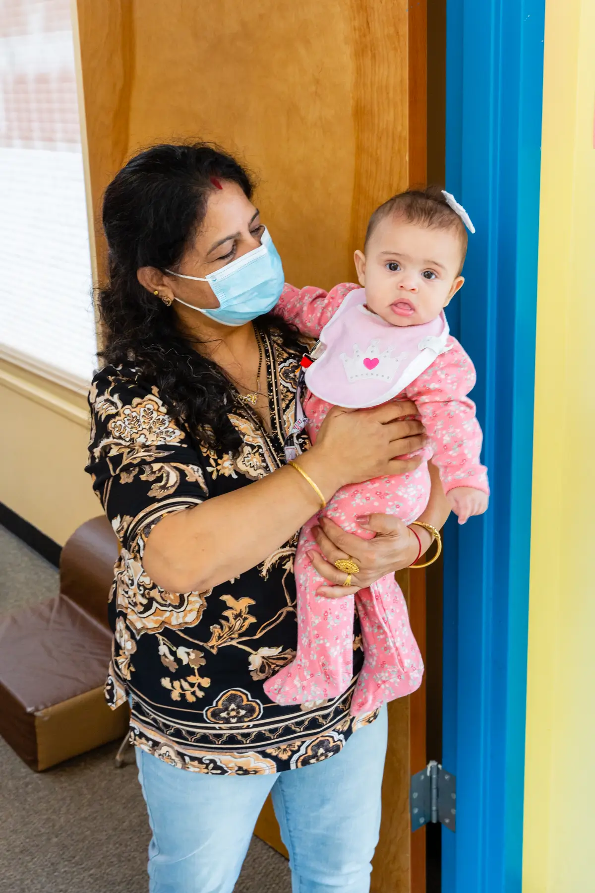 Woman holding a baby wearing a mask indoors.
