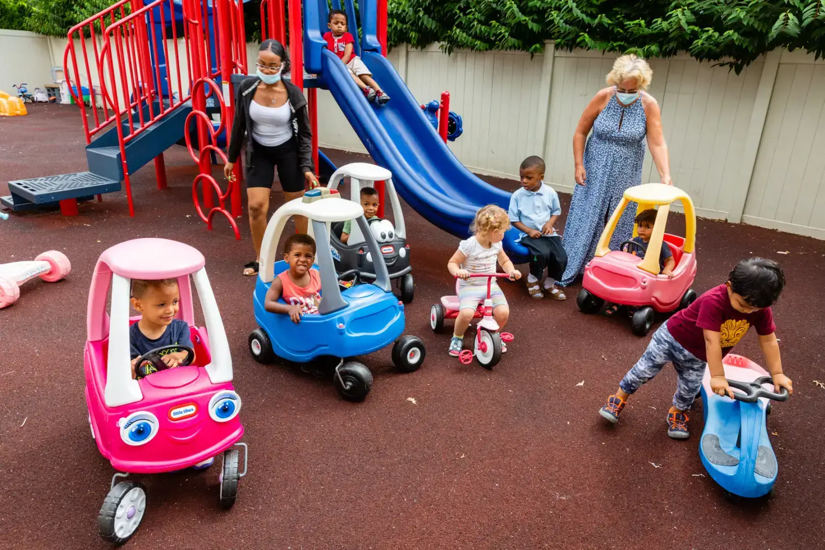 Children playing with toy cars and bikes in a playground.